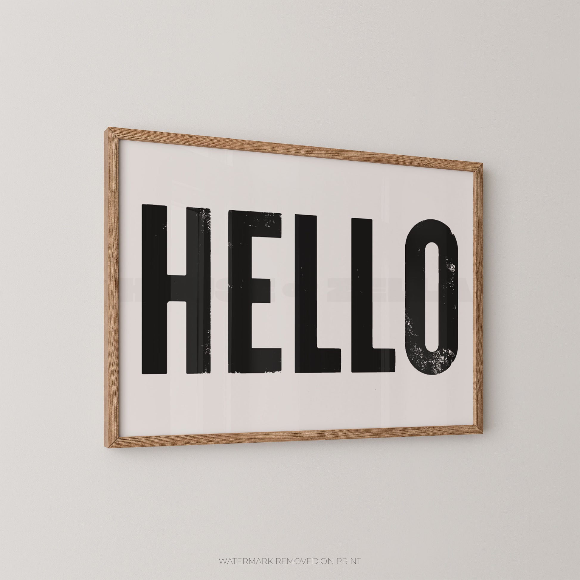 Framed wall art print with the word “HELLO” in large black block letters on a white background, shown hanging on a light gray wall.