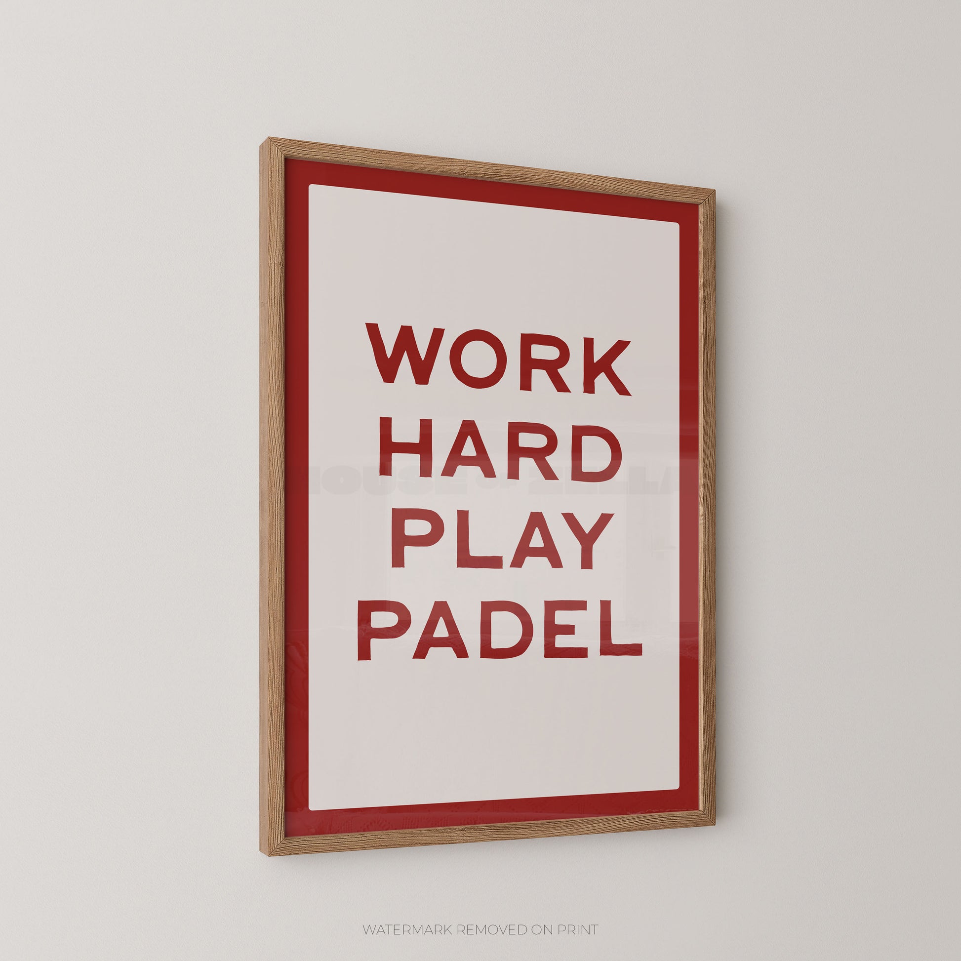 "Work Hard Play Padel bold typography sports wall art print with red lettering on a cream background with a red border, displayed at an angle in an oak frame"


