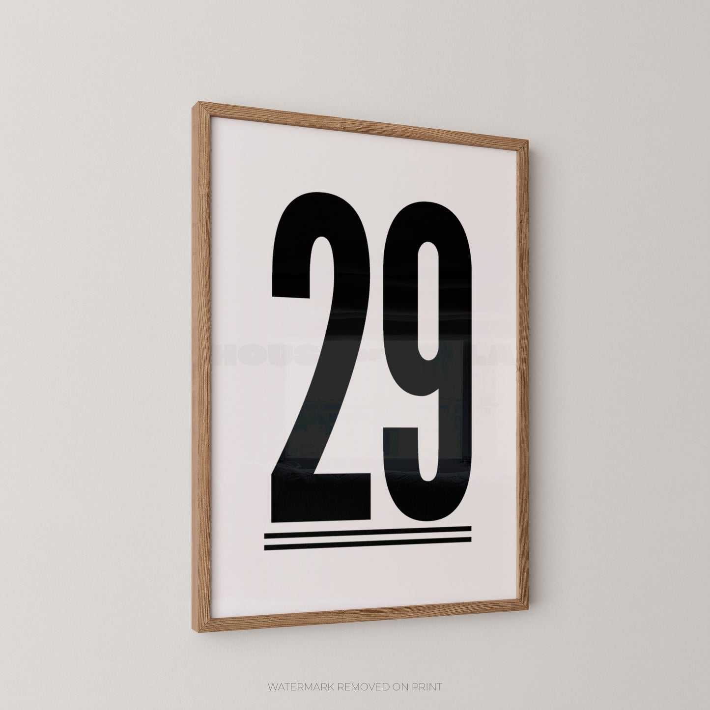 A minimalist framed art print featuring the bold black number '29' on a white background, enclosed in a light natural wood frame and mounted on a neutral light gray wall.
