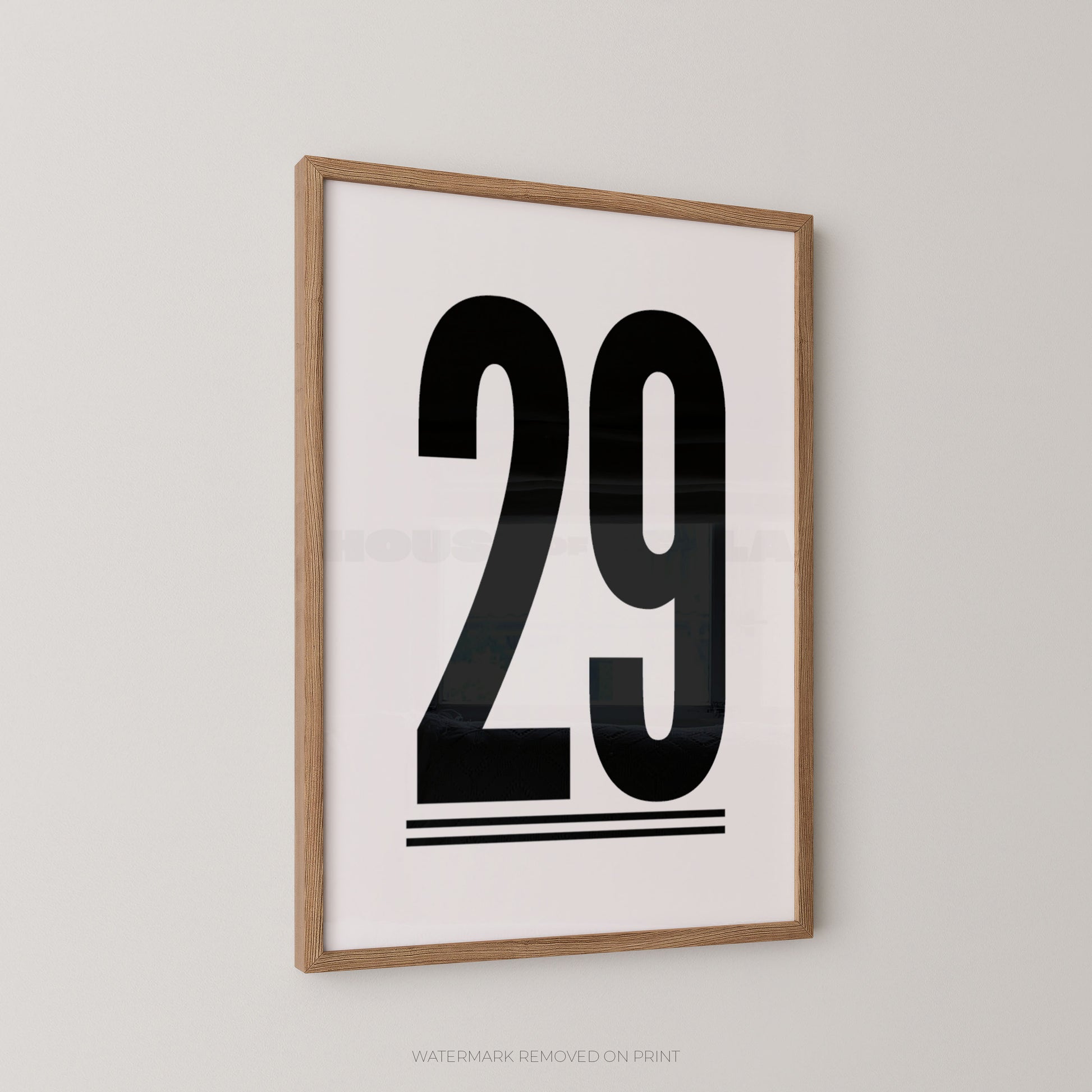 A minimalist framed art print featuring the bold black number '29' on a white background, enclosed in a light natural wood frame and mounted on a neutral light gray wall.