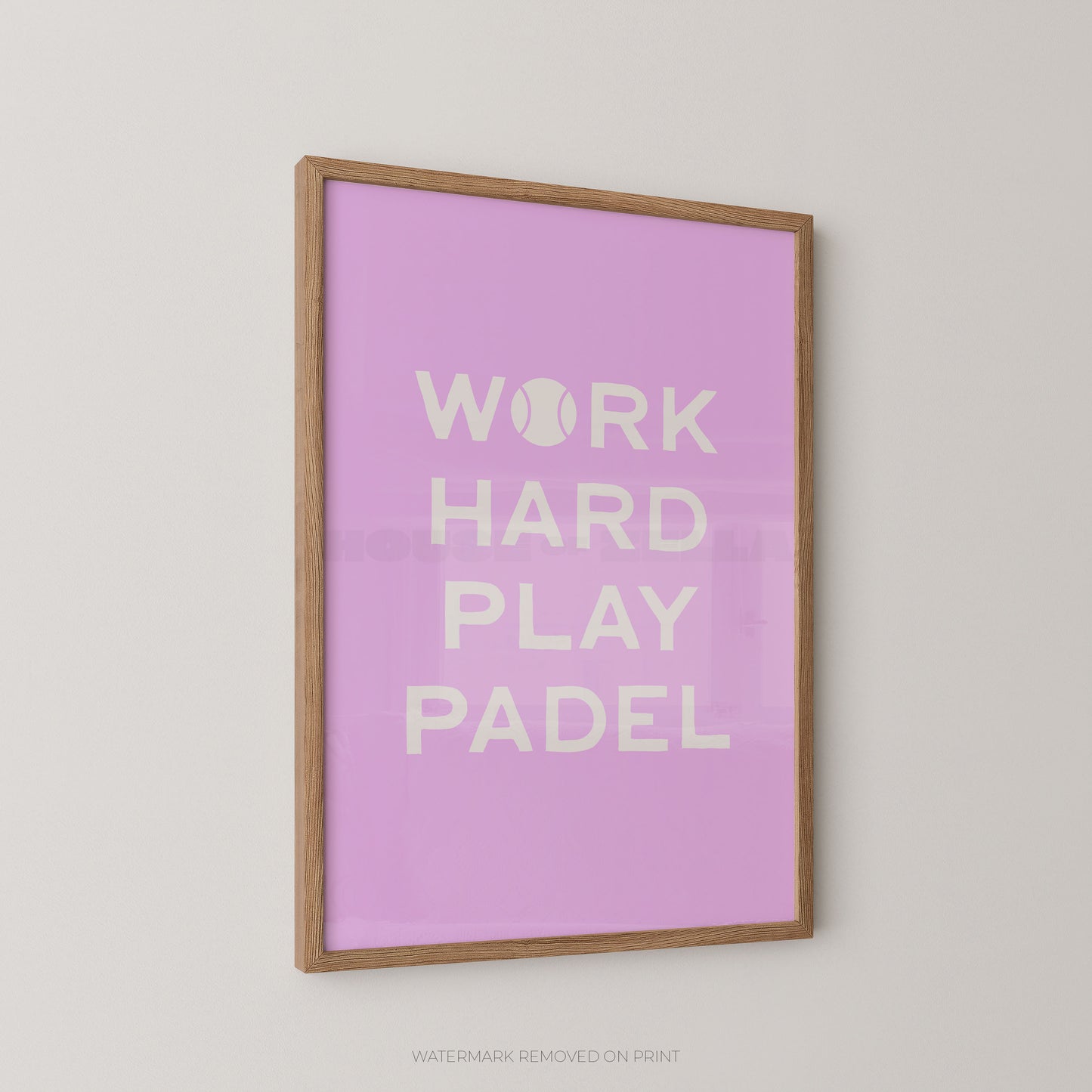 A framed wall art print with a light wood frame and a pink background, featuring the text 'WORK HARD PLAY PADEL' in white. The print is mounted on a light gray wall.
