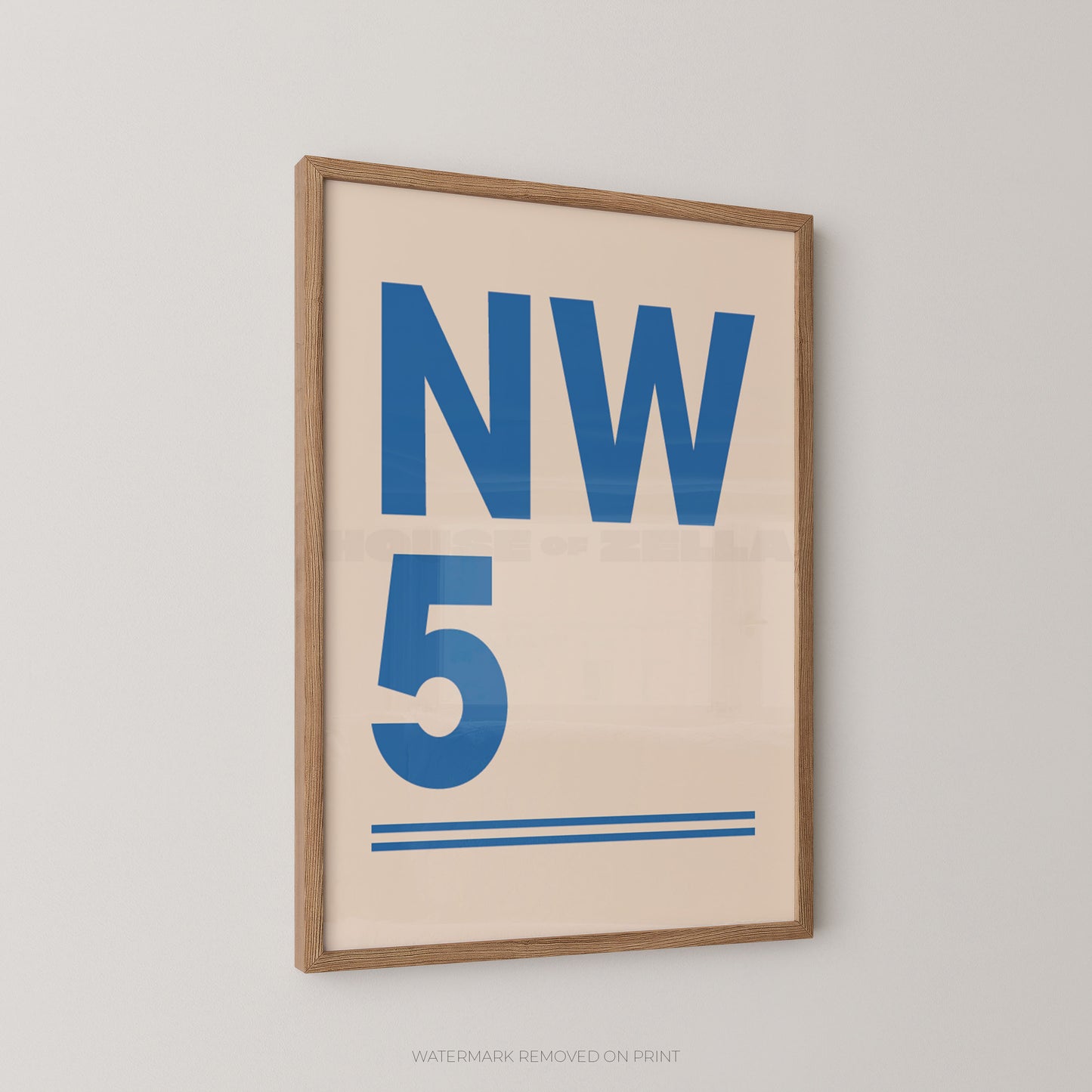 A framed minimalist postcode art print featuring the text 'NW 5' in blue on a warm cream background, enclosed in a light natural wood frame and mounted on a neutral light gray wall.