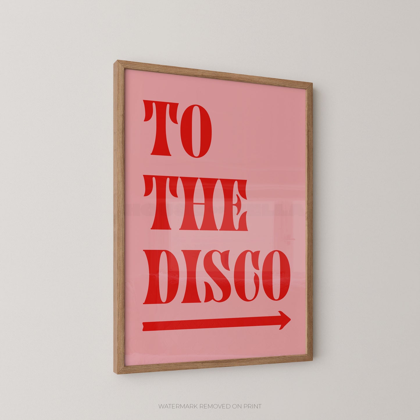 Framed wall art print with the words “TO THE DISCO” in large red letters on a pink background, with a red arrow beneath. The print is shown hanging on a light gray wall.