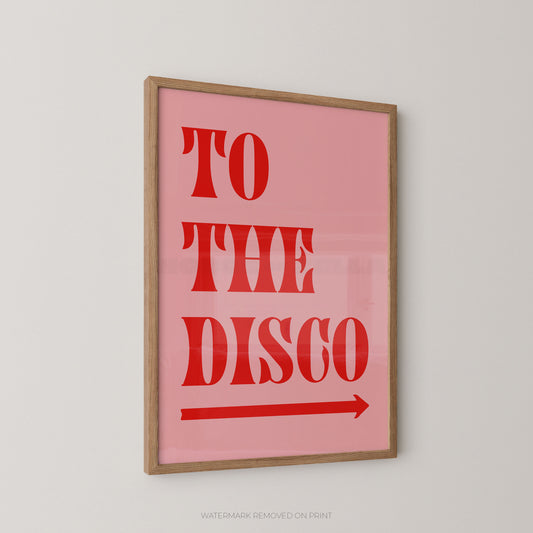 Framed wall art print with the words “TO THE DISCO” in large red letters on a pink background, with a red arrow beneath. The print is shown hanging on a light gray wall.