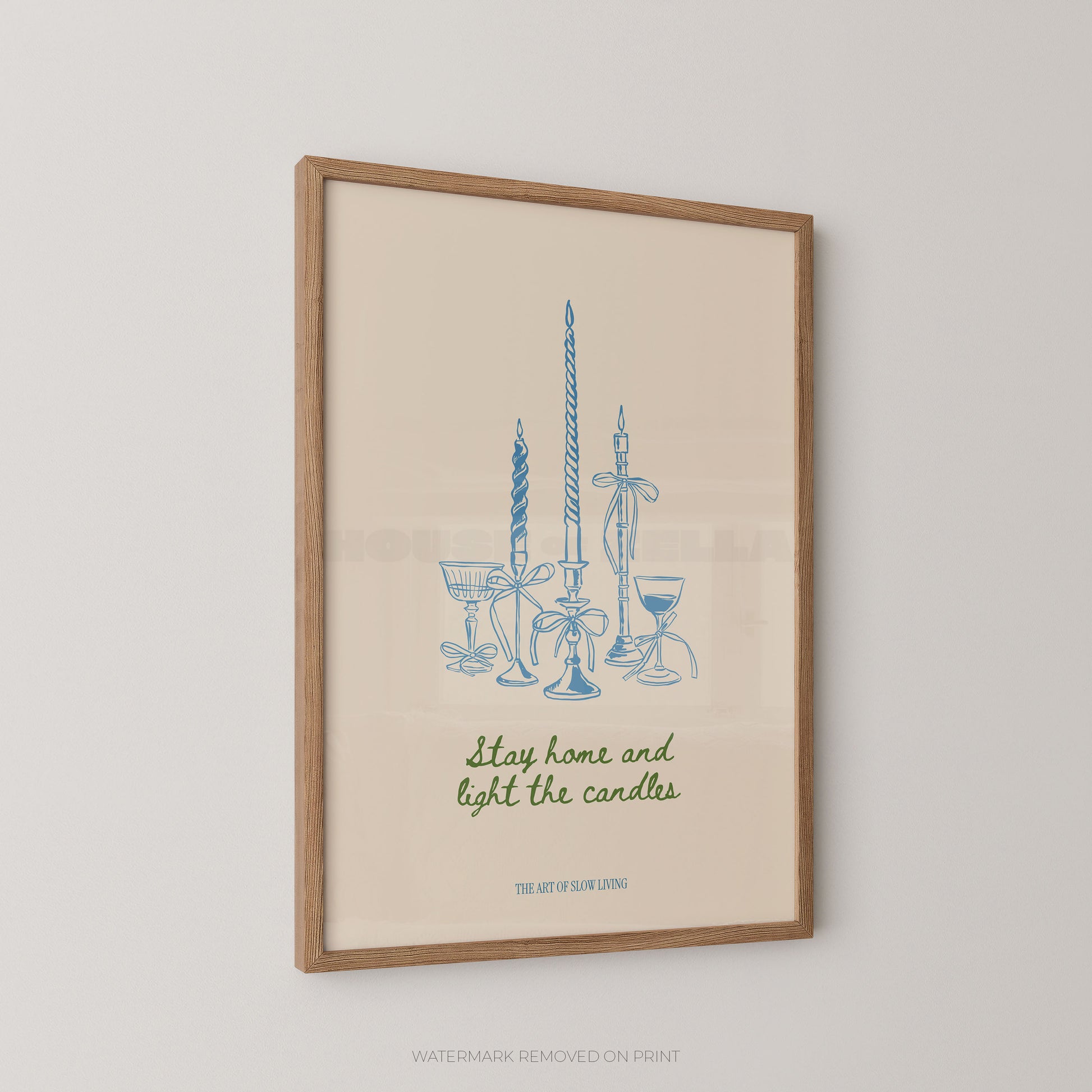 Framed art print featuring a blue line drawing of candles and glassware with the phrase 'Stay home and light the candles' in green script, displayed against a light neutral wall.