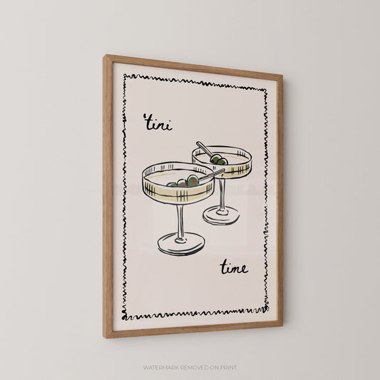 Framed wall art print featuring a minimalist illustration of two cocktail glasses with olives and the words 'tini time' in black script, shown hanging on a light gray wall.