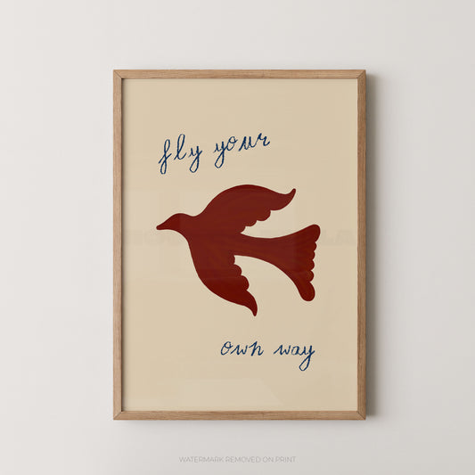 Framed wall art print with a beige background, a dark red dove silhouette in the center, and the phrase 'fly your own way' in blue script, shown in a light wood frame against a light gray wall.