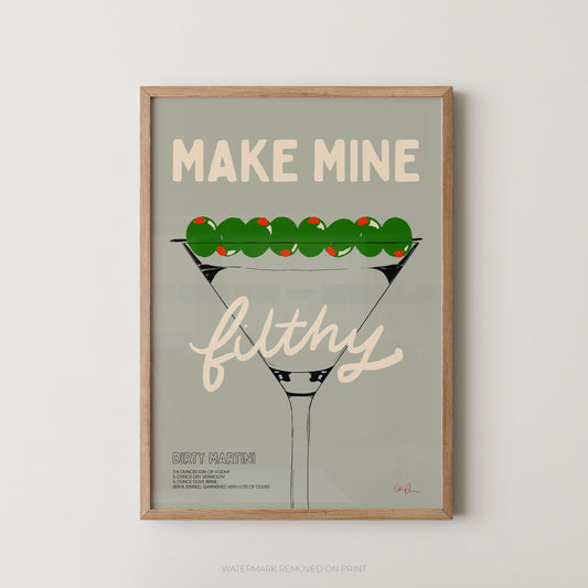 A framed art print featuring a stylized martini glass with olives and the text 'MAKE MINE filthy' on a muted sage background, shown against a light neutral wall.