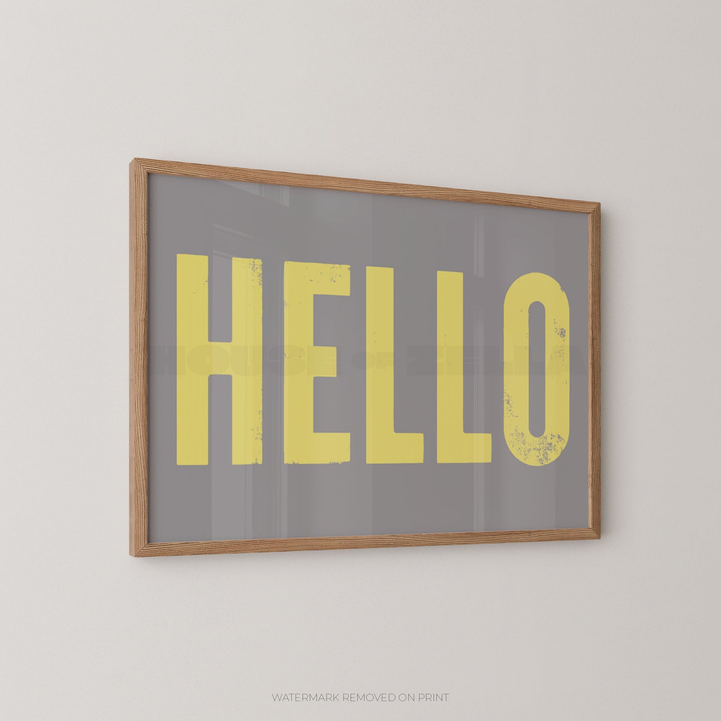Framed wall art print with the word 'HELLO' in large yellow letters on a gray background, mounted on a light beige wall.