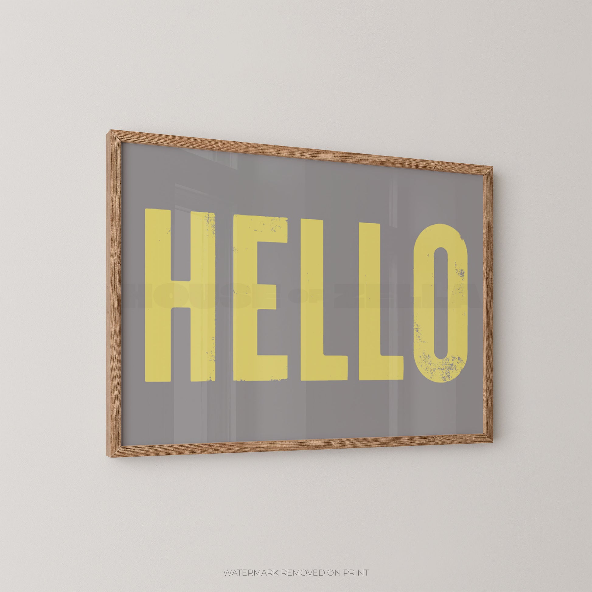 Framed wall art print with the word 'HELLO' in large yellow letters on a gray background, mounted on a light beige wall.