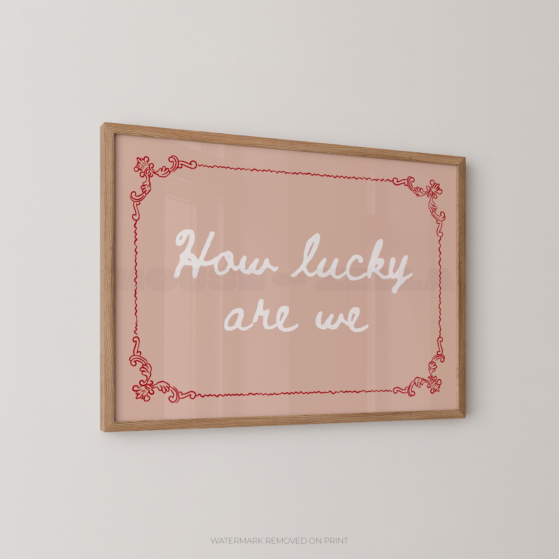 A framed wall art print with the phrase “How lucky are we” in white script inside a red decorative border, mounted on a light gray wall.