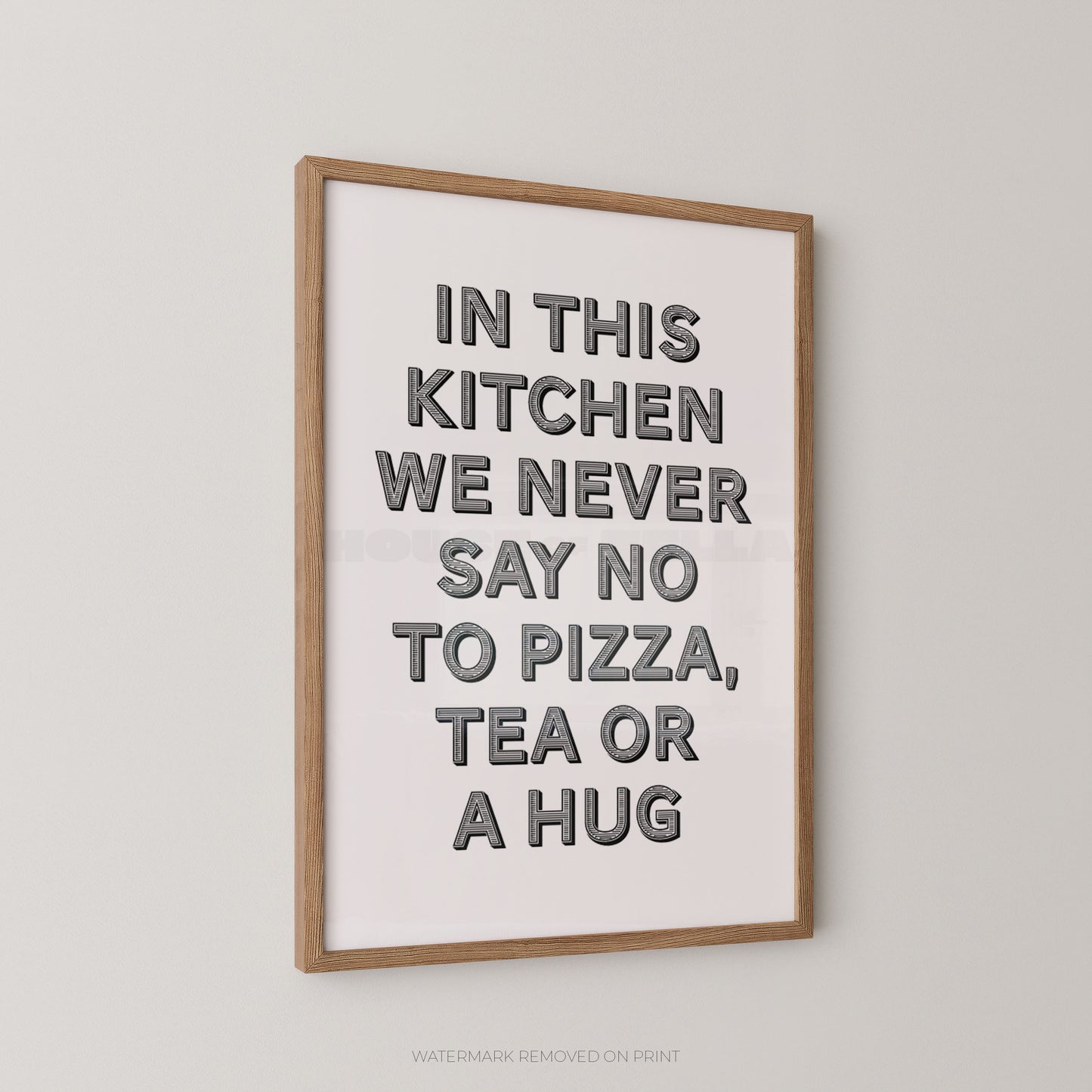 Framed typographic wall art hanging on a light gray wall, with a light wood frame and bold dark gray text reading, 'IN THIS KITCHEN WE NEVER SAY NO TO PIZZA, TEA OR A HUG.'.