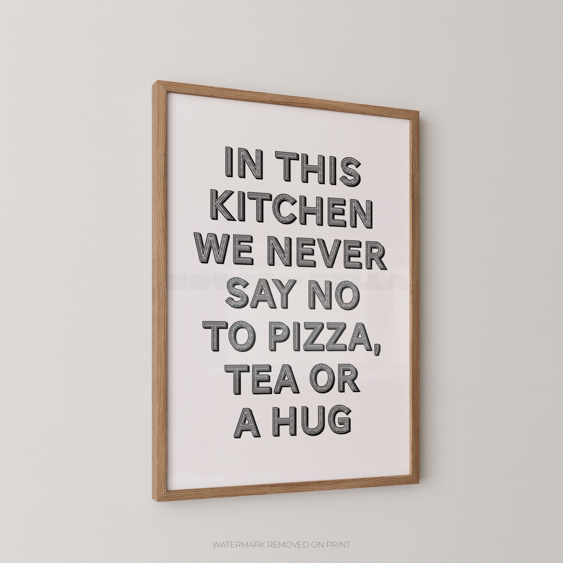 Framed typographic wall art hanging on a light gray wall, with a light wood frame and bold dark gray text reading, 'IN THIS KITCHEN WE NEVER SAY NO TO PIZZA, TEA OR A HUG.'.