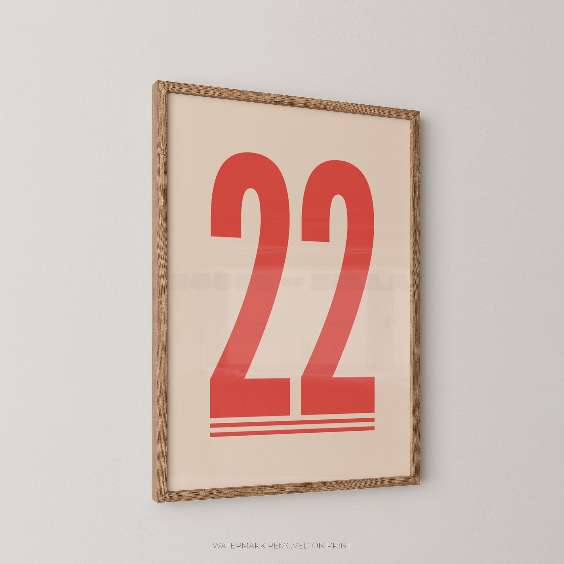 Framed minimalist wall art print featuring the red number 22 on a warm cream background, enclosed in a light natural wood frame and shown hanging on a light gray wall.
