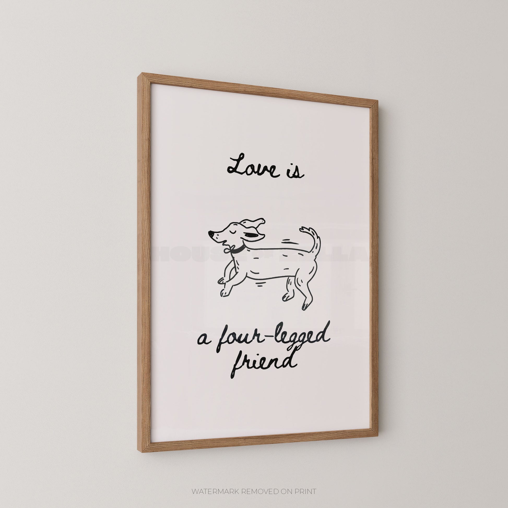Framed wall art print with a light wood frame, featuring a simple black line drawing of a dog and the handwritten text 'Love is a four-legged friend' on a white background, shown hanging on a light gray wall.