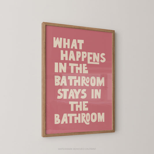 Funny bathroom wall art print in a wood frame – bold cream chunky typography reading "What Happens In The Bathroom Stays In The Bathroom" on a dusky pink background