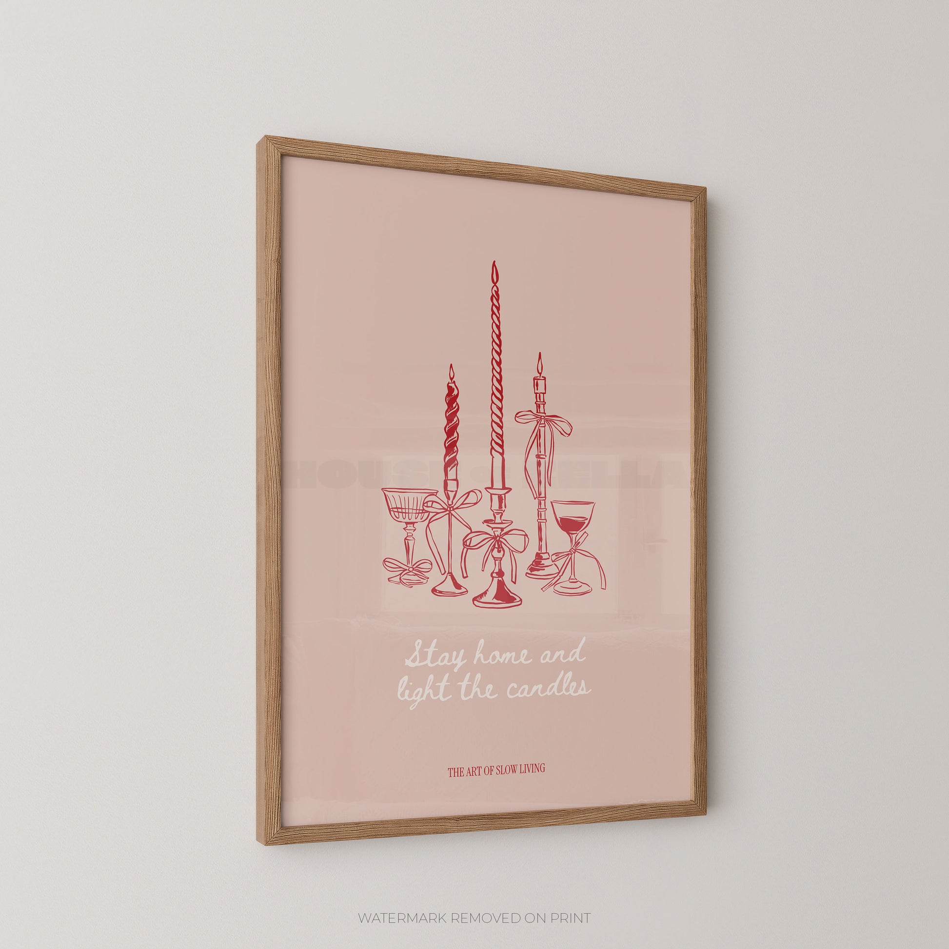 Framed art print featuring a minimalist red line drawing of candles, goblets, and a glass with the text 'stay home and light the candles' on a soft pink background, shown hanging on a light gray wall.
