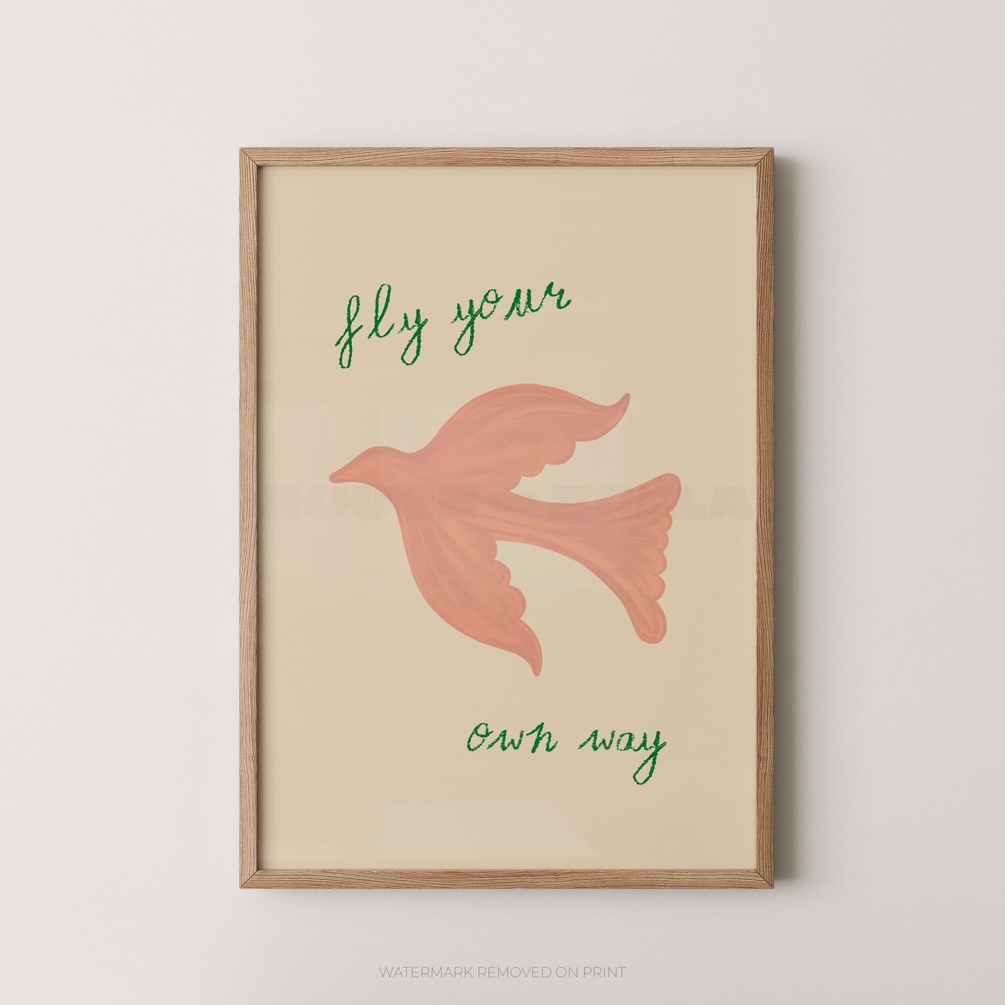Framed wall art print with a light wood frame, featuring a pink bird illustration and the handwritten phrase 'fly your own way' on a warm cream background.