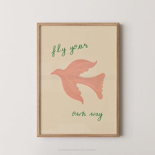Framed wall art print with a light wood frame, featuring a pink bird illustration and the handwritten phrase 'fly your own way' on a warm cream background.