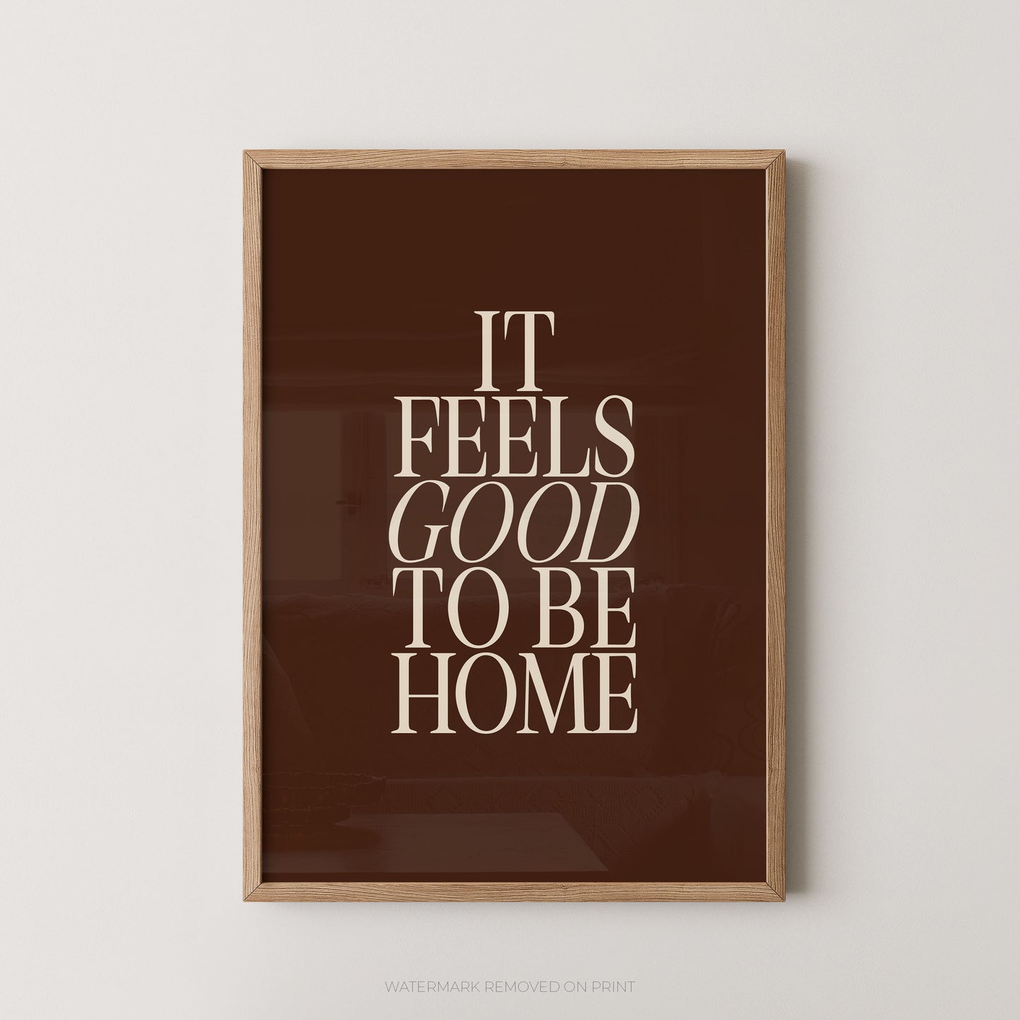 "It Feels Good To Be Home typography wall art print with elegant serif lettering in cream on a rich chocolate brown background, displayed straight-on in an oak frame"

