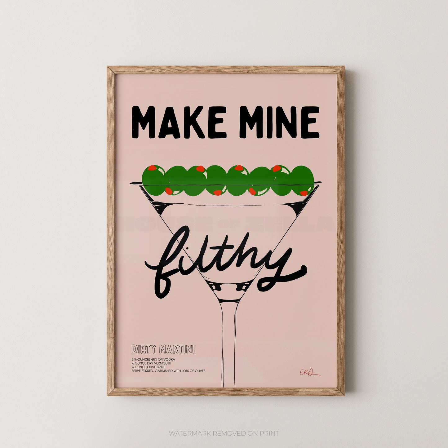 A framed typographic art print featuring a martini glass with green olives on top and the text 'MAKE MINE filthy' on a pale pink background, shown against a light neutral wall.