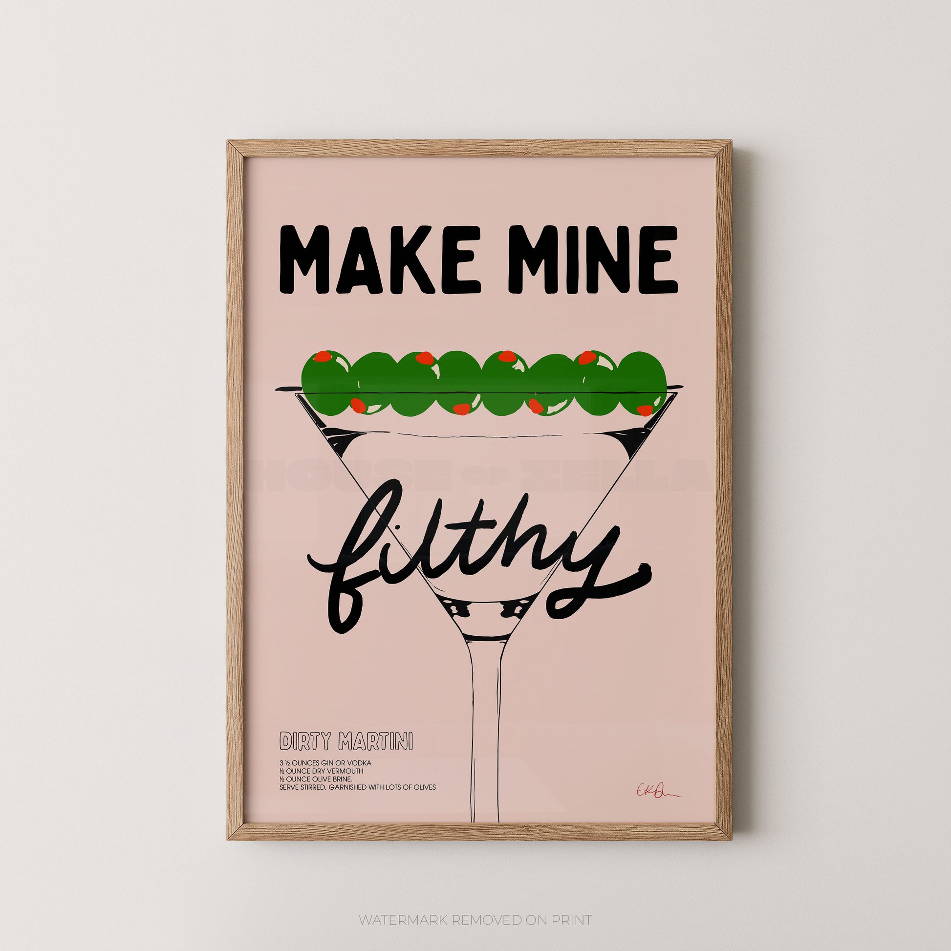 A framed typographic art print featuring a martini glass with green olives on top and the text 'MAKE MINE filthy' on a pale pink background, shown against a light neutral wall.