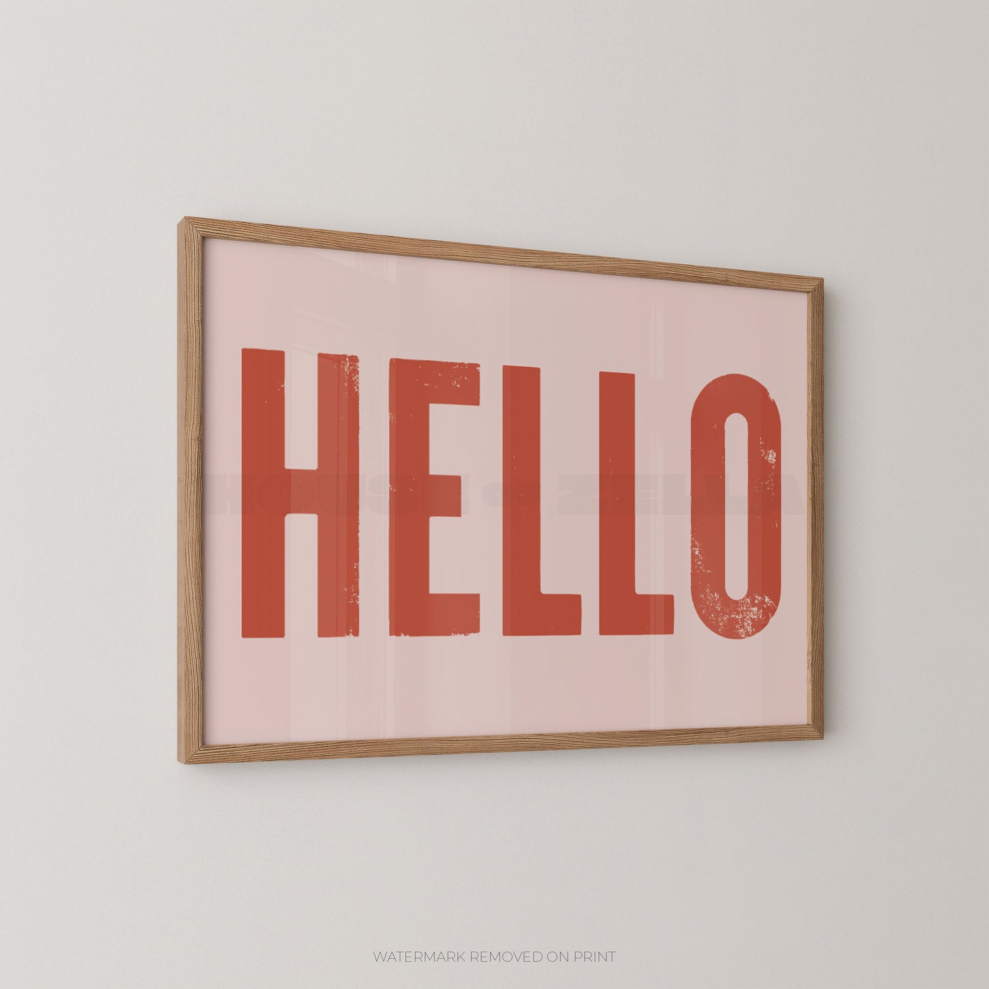 Framed typographic wall art with the word "HELLO" in large distressed red letters on a pale pink background, shown hanging on a light neutral wall.