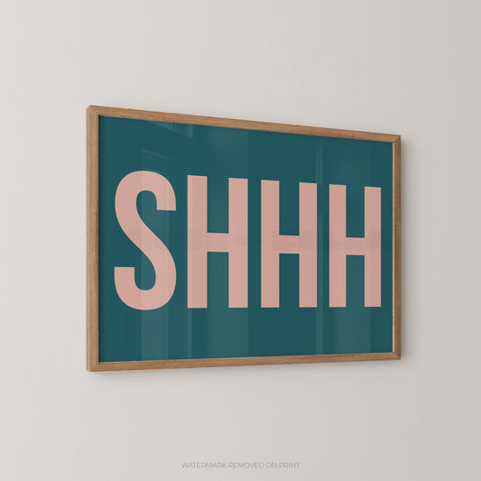 Framed typographic wall art with the word “SHHH” in large pink letters on a teal background, shown hanging on a light neutral wall.