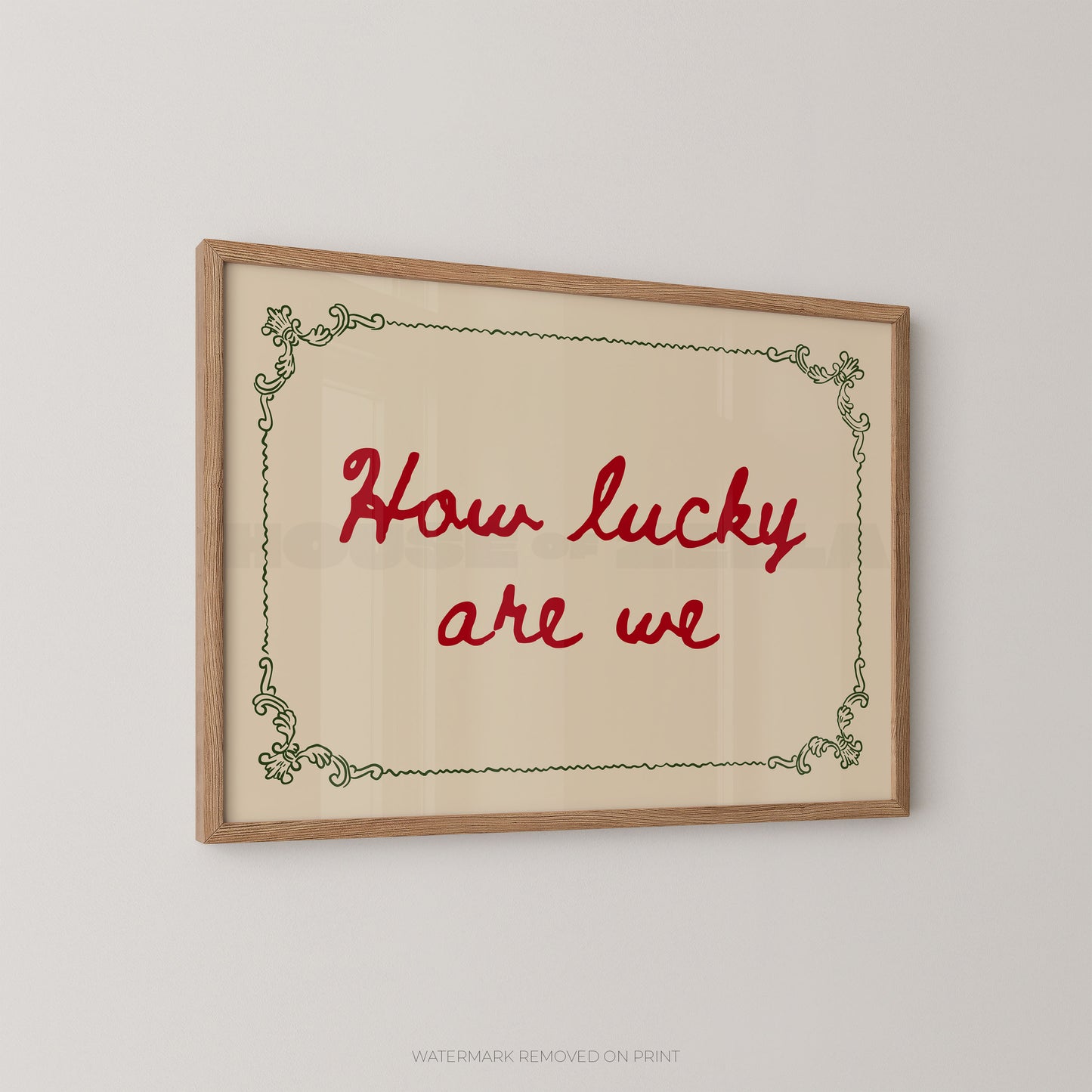 A framed typographic wall art print with the phrase “How lucky are we” in red script, set within a light wood frame and a pale cream background, shown hanging on a light gray wall.