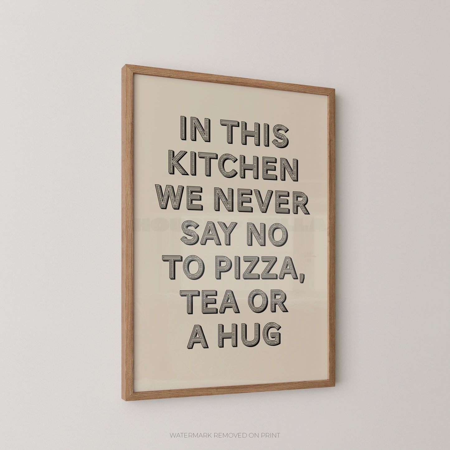 A framed typographic wall art print with a cream background and black raised lettering that reads, 'IN THIS KITCHEN WE NEVER SAY NO TO PIZZA, TEA OR A HUG,' shown hanging on a light neutral wall.