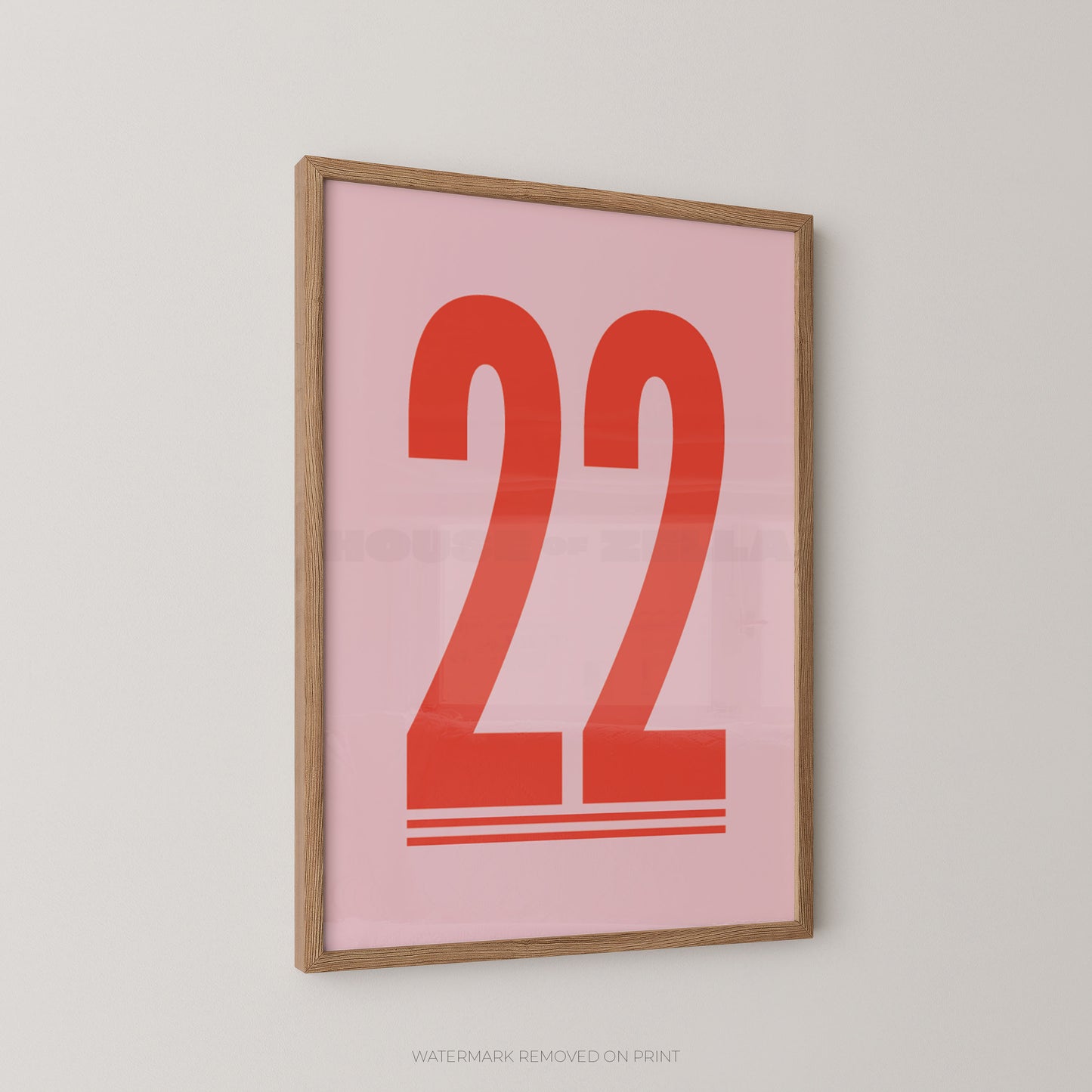Framed minimalist wall art print featuring the number 22 in red on a light pink background, mounted on a light gray wall.