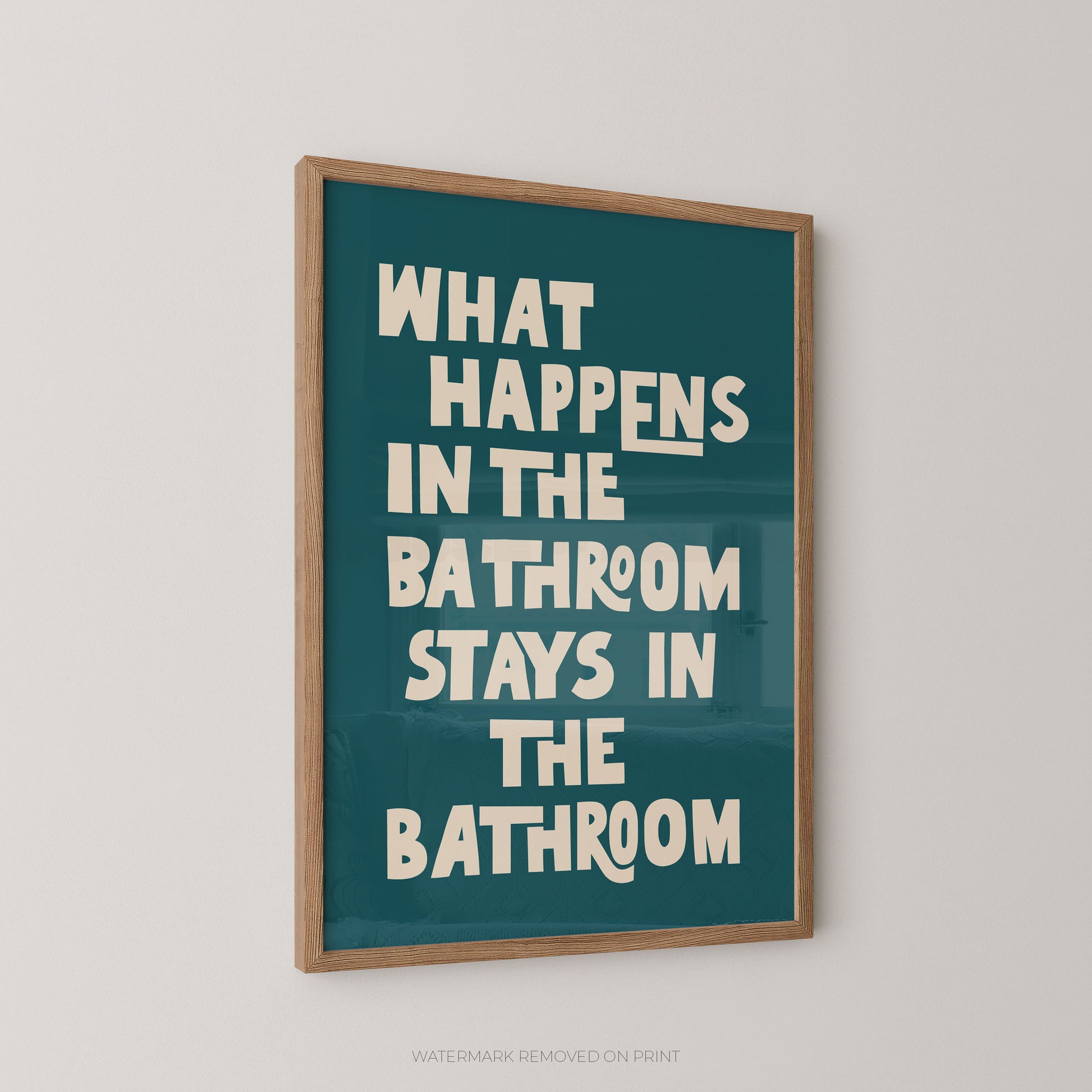 Funny bathroom wall art print in a wood frame – playful chunky cream typography on a teal background reading "What Happens In The Bathroom Stays In The Bathroom"