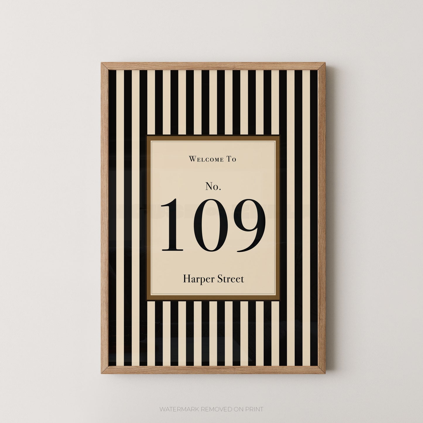 Framed wall art print with vertical black and cream stripes, featuring a central cream panel with the text 'Welcome To No. 109 Harper Street' in black serif lettering, shown against a light neutral wall.
