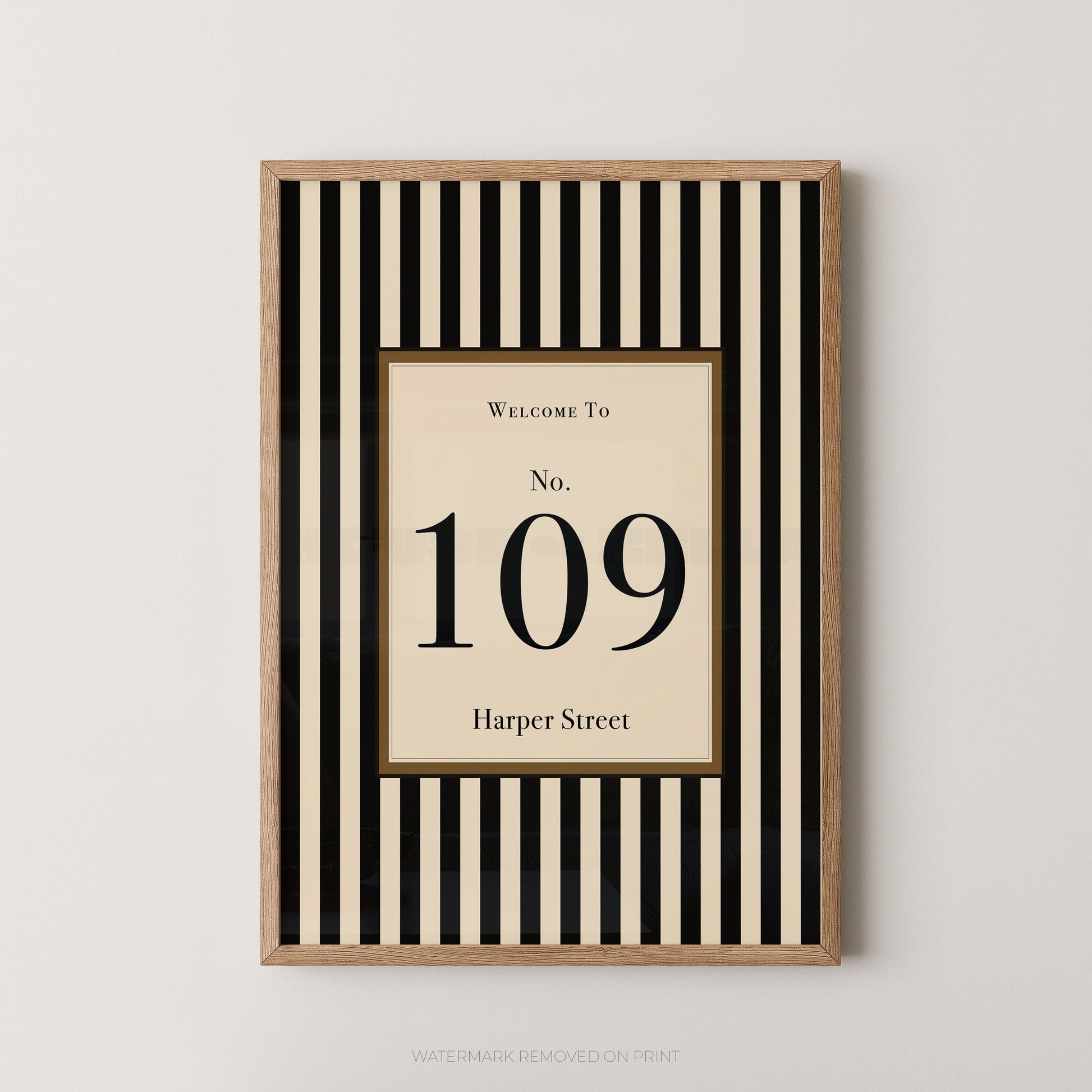 Framed wall art print with vertical black and cream stripes, featuring a central cream panel with the text 'Welcome To No. 109 Harper Street' in black serif lettering, shown against a light neutral wall.