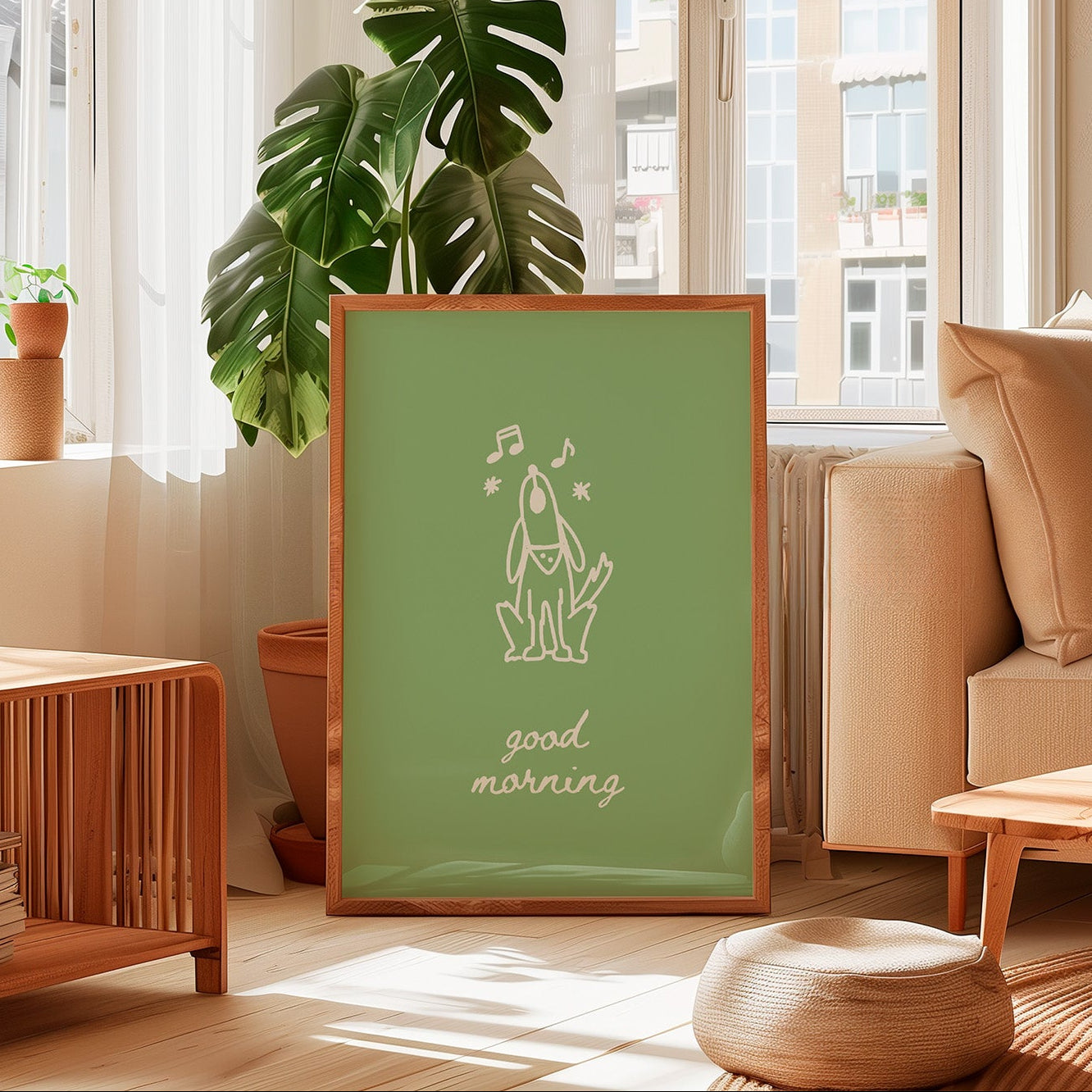 A framed art print with a sage green background and a white line drawing of a frog with musical notes and the text 'good morning' is displayed in a bright, modern living room setting.