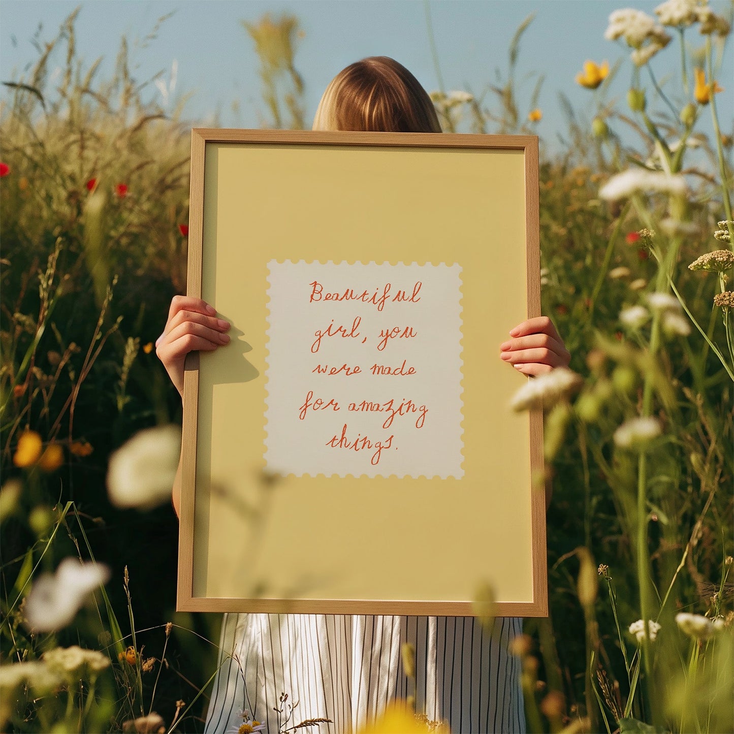 Person holding a framed quote in a field of flowers