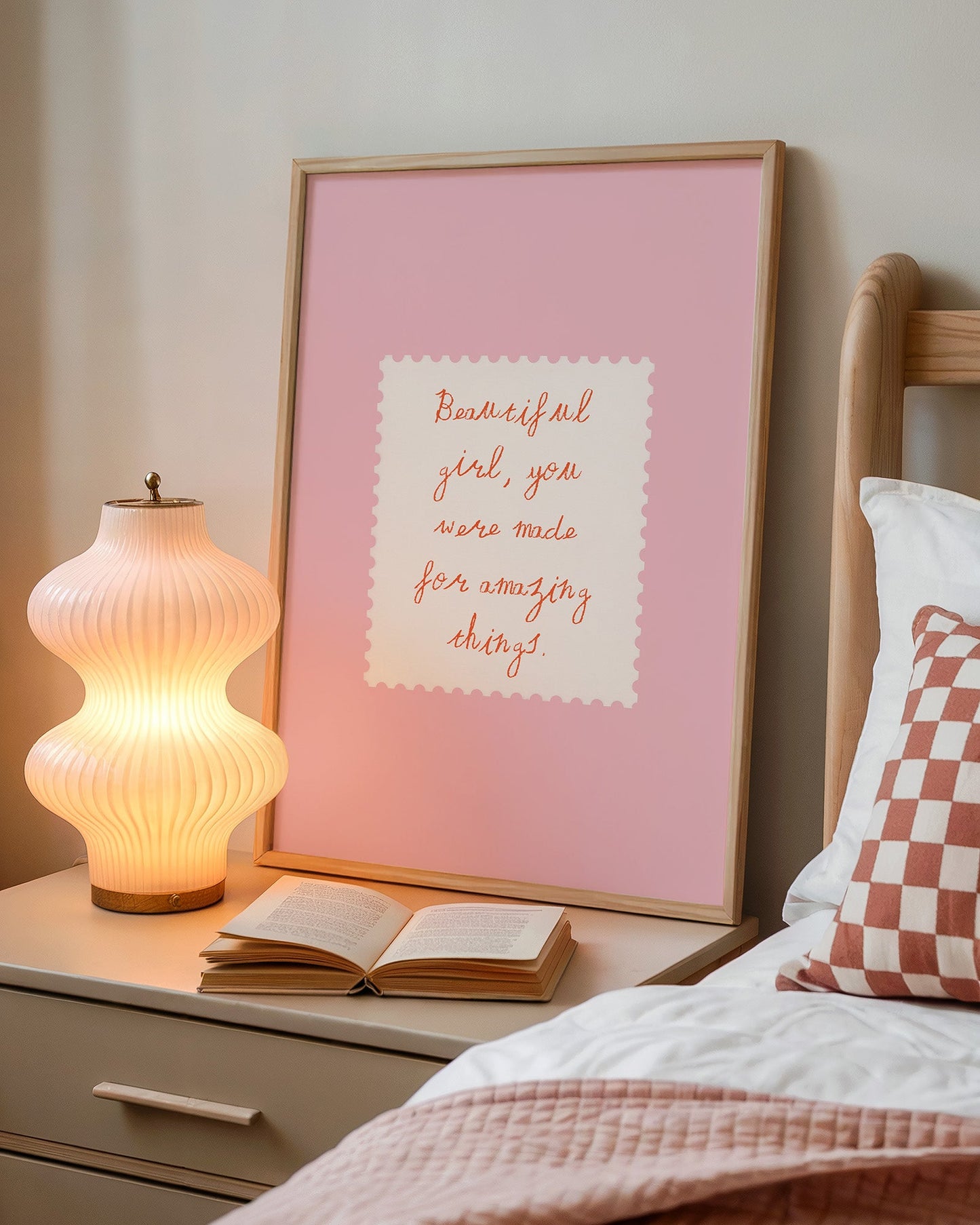 Framed motivational quote on a bedside table with a lamp and open book.